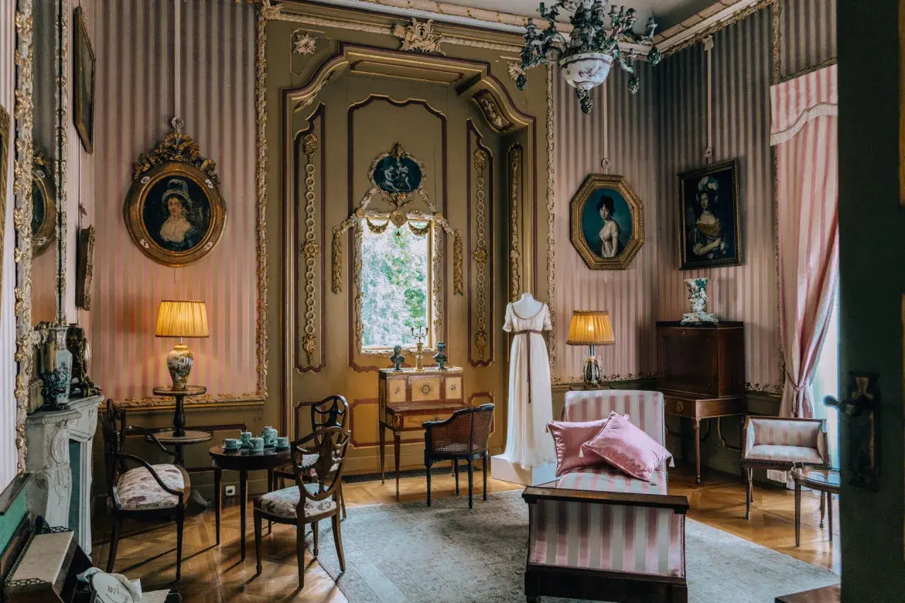 Eleganckie wnętrze pałacu w Nieborowie z portretami dam, manekinem w sukni i zabytkowymi meblami.