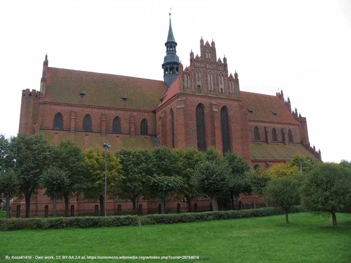 Gotycka katedra w Pelplinie, ceglana budowla z charakterystyczną wieżą i strzelistymi oknami, otoczona zielenią.