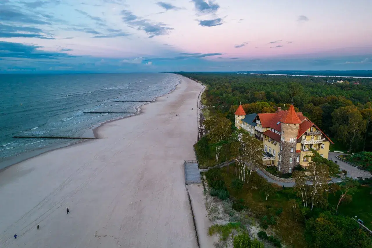 Zachód słońca nad morzem w Łebie. Piękna plaża, las i zabytkowy budynek przypominający zamek.