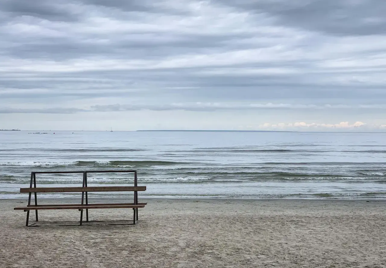 Pusta ławka na plaży w Gąskach, wpatrzona w spokojne morze pod zachmurzonym niebem.