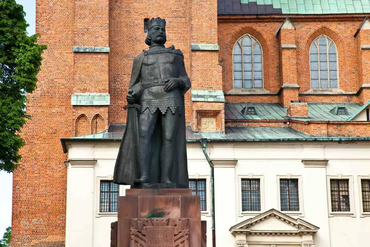 Pomnik Bolesława Chrobrego, pierwszego króla polskiego, na tle ceglanej katedry.