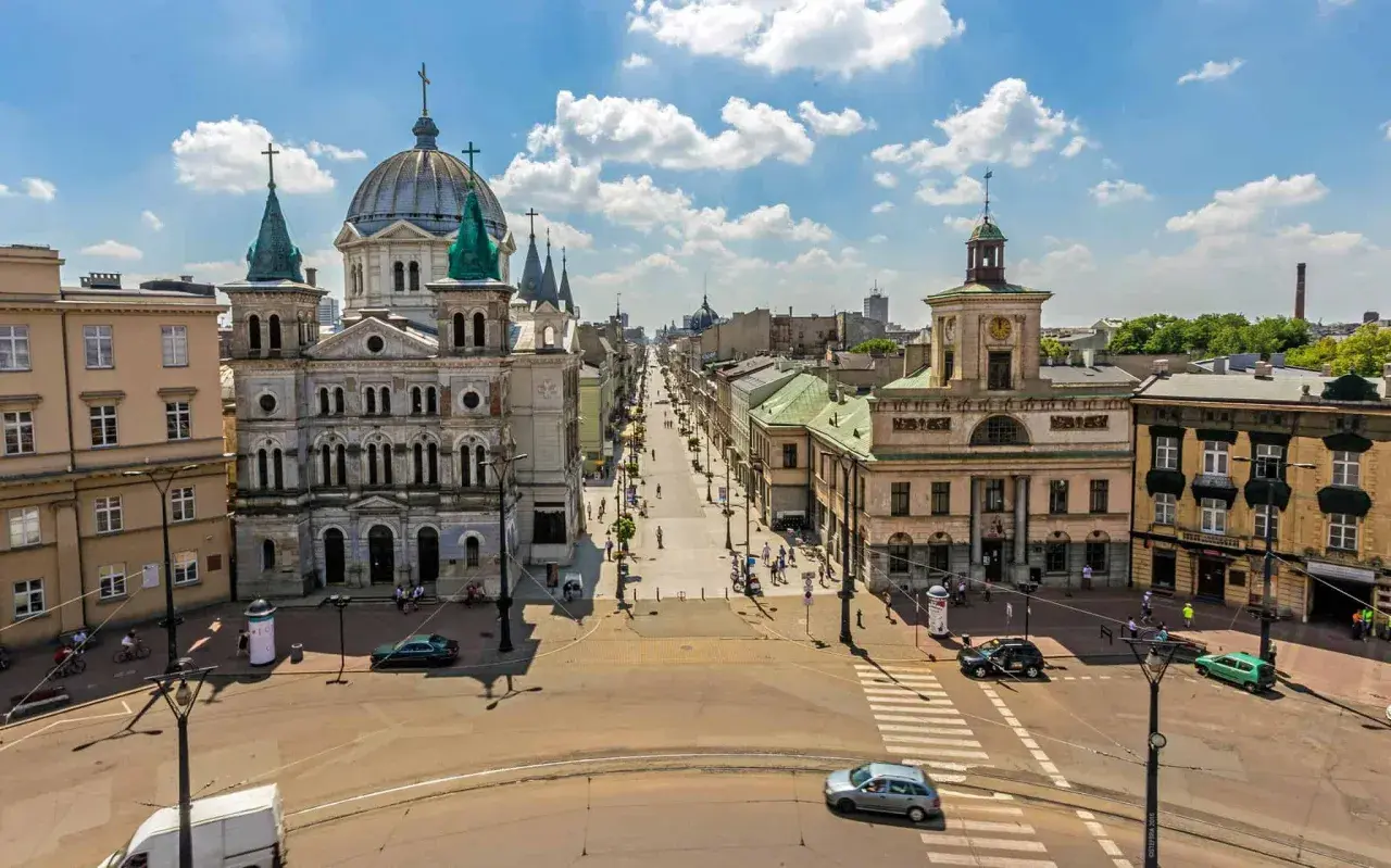 Widok na plac wolności w Łodzi z monumentalną katedrą po lewej i długą ulicą pełną ludzi i samochodów.