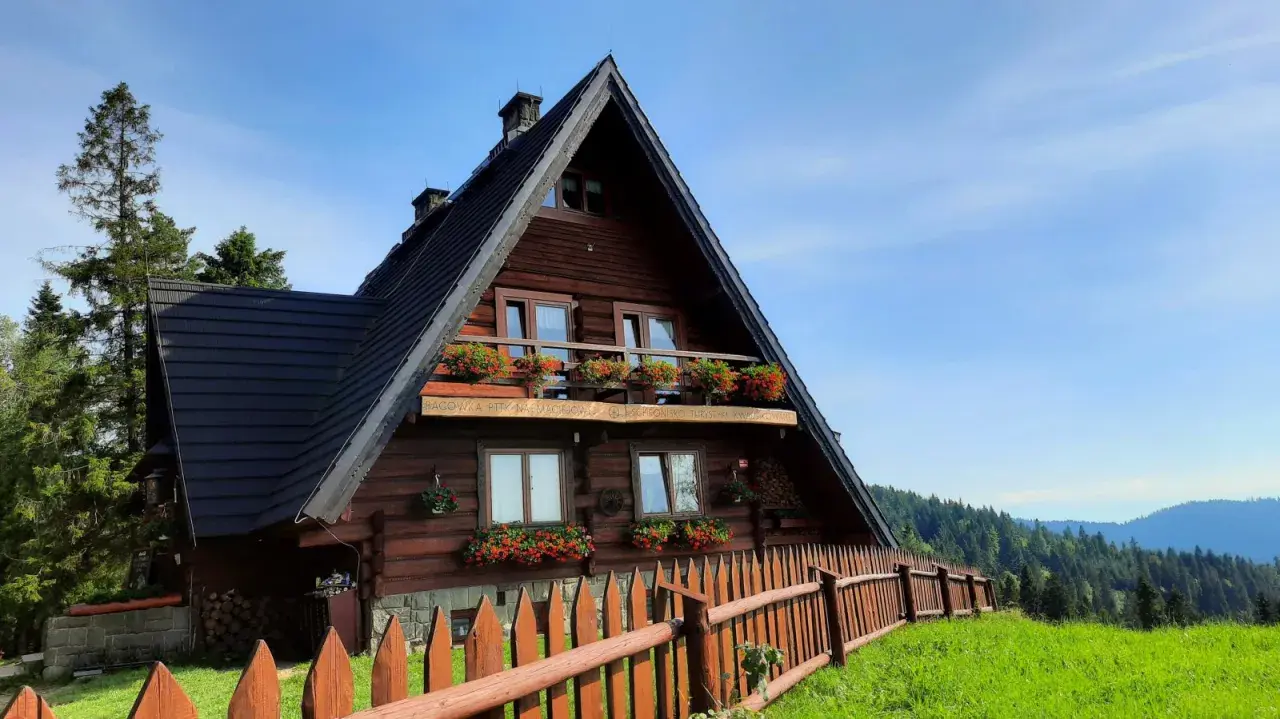 Drewniane schronisko na Maciejowej z kwitnącymi pelargoniami na balkonach i oknach. Otoczone zielenią i lasem, zaprasza na górskie wędrówki.