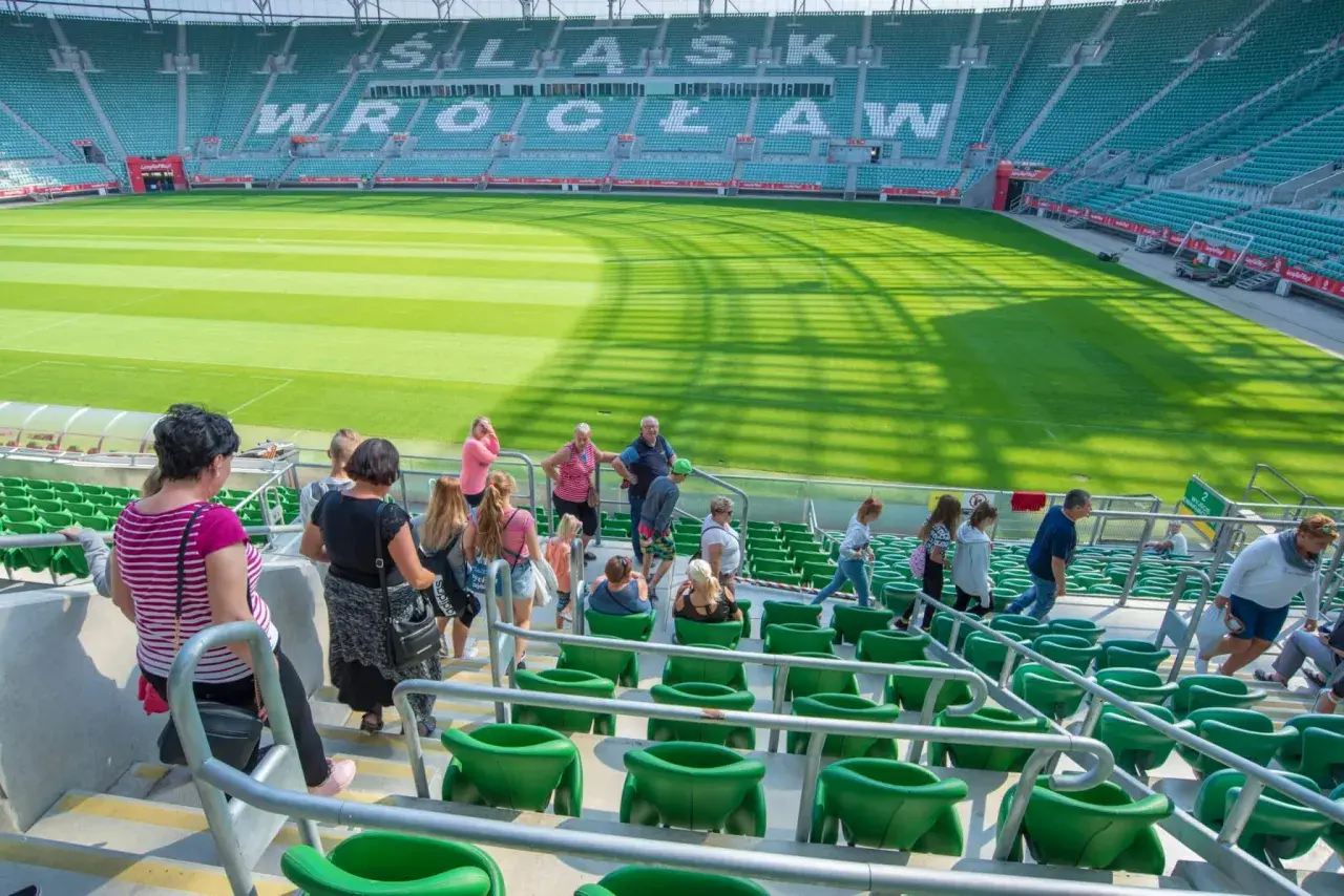 Grupa ludzi wchodzi na zielone trybuny stadionu. W tle widać murawę i napis "WROCŁAW".