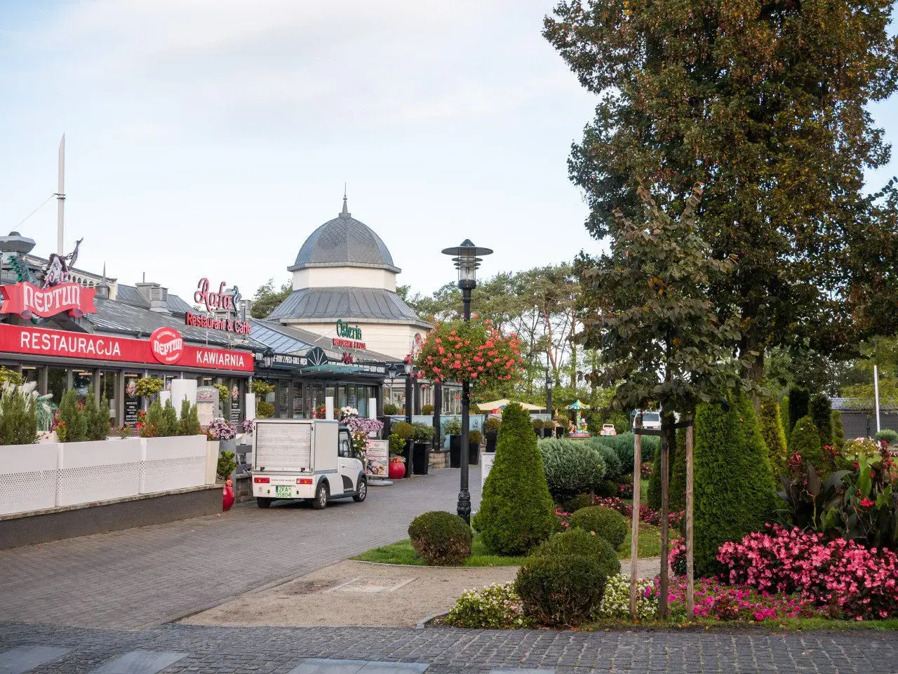 Spacer po alei gwiazd w Międzyzdrojach, z restauracjami i kawiarniami po lewej stronie, a zielenią i drzewami po prawej.