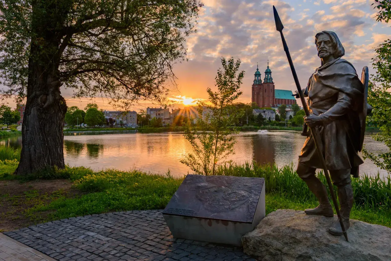 Pomnik wojownika na tle jeziora i katedry. Wschód słońca nad Gnieznem, pierwszą stolicą Polski.