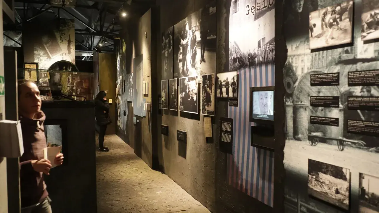 Wystawa w Muzeum Powstania Warszawskiego. Zwiedzający wpatrują się w historyczne fotografie i eksponaty, które budzą refleksje.