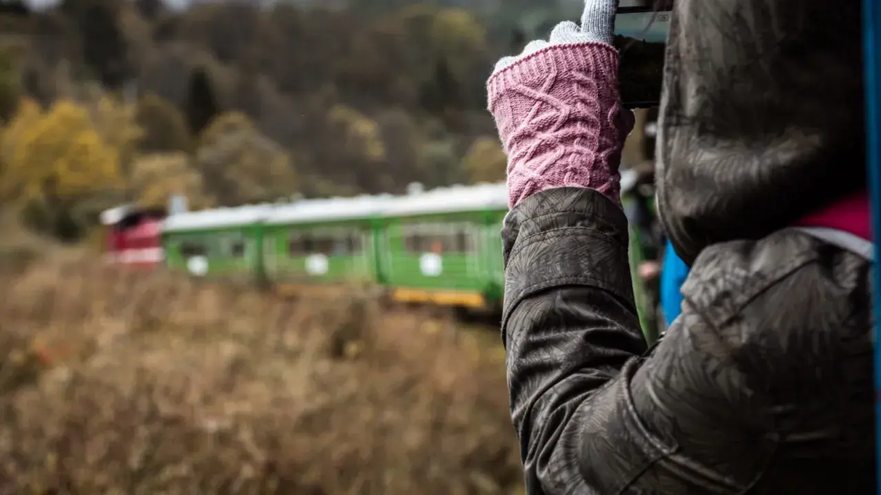 Osoba w różowych rękawiczkach fotografuje zielono-czerwony pociąg. Która kolejka bieszczadzka, która trasa ciekawsza?