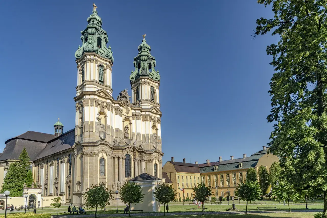 Barokowy zespół klasztorny w Krzeszowie z dwiema wieżami i rozległym skrzydłem, otoczony zielenią.