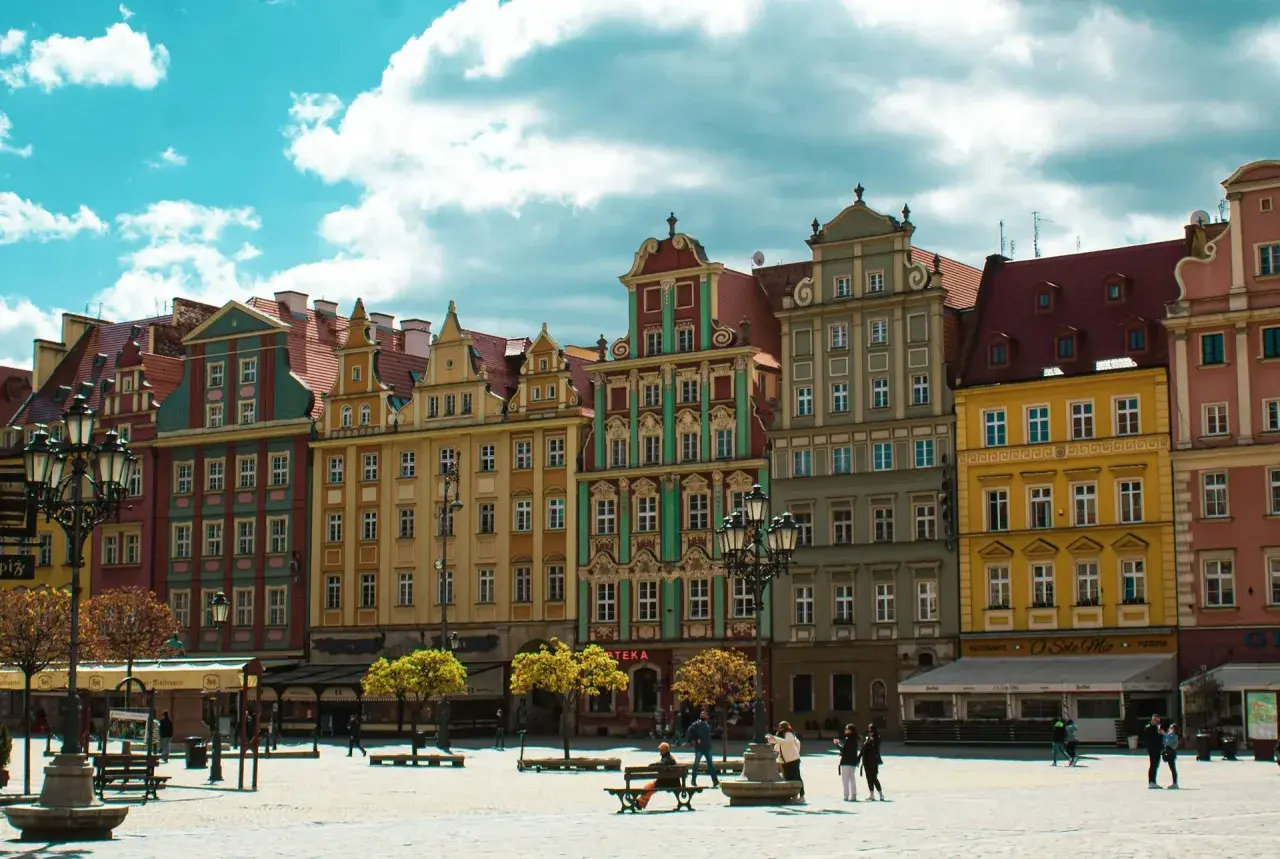 Kolorowe kamienice na starym rynku we Wrocławiu, z błękitnym niebem i białymi chmurami w tle.