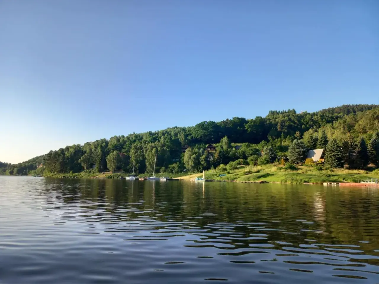 Spokojne jezioro Rożnowskie z łodziami przy brzegu, otoczone zielonymi wzgórzami. Idealne miejsce na wypoczynek i odkrywanie atrakcji.