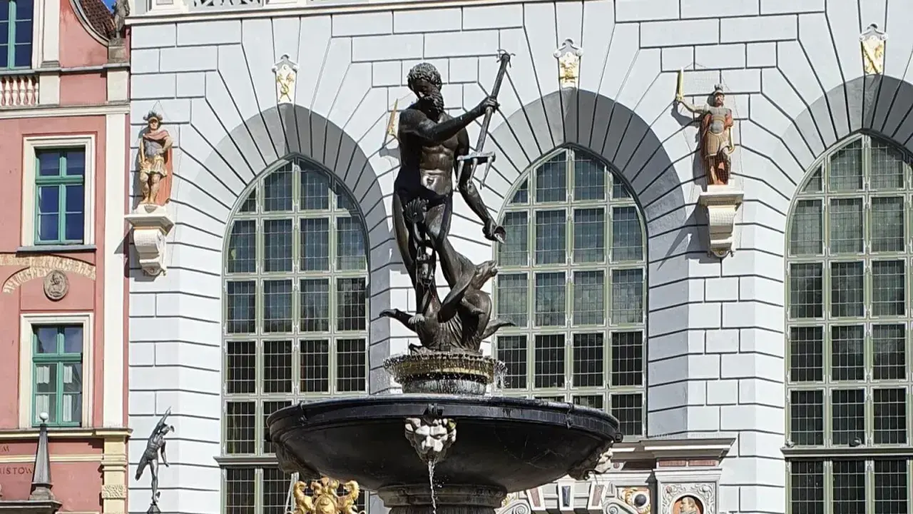 Fontanna Neptuna znajduje się w Gdańsku, przed fasadą budynku z arkadowymi oknami. Rzeźba przedstawia boga mórz na tle kamiennej architektury.