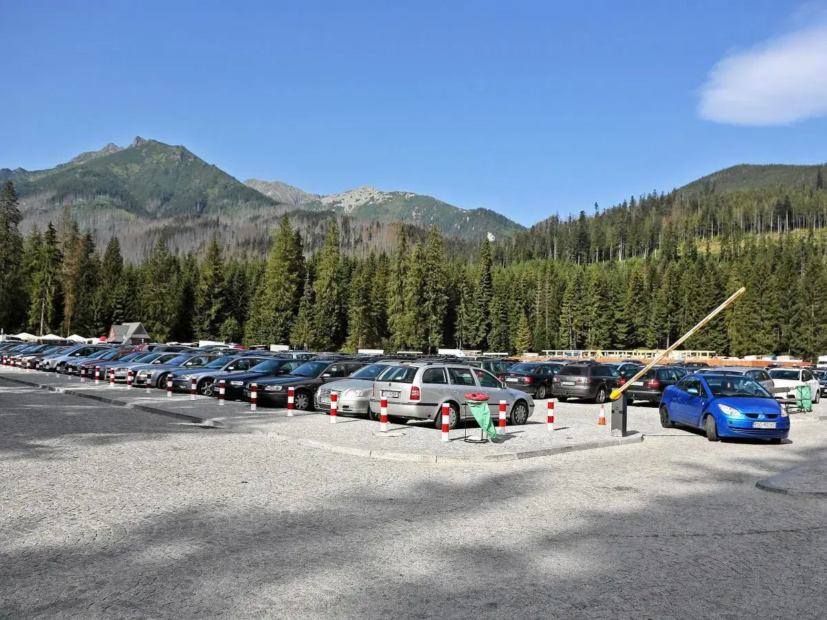 Parking pod Morskim Okiem, pełen samochodów, z górami i lasem w tle.