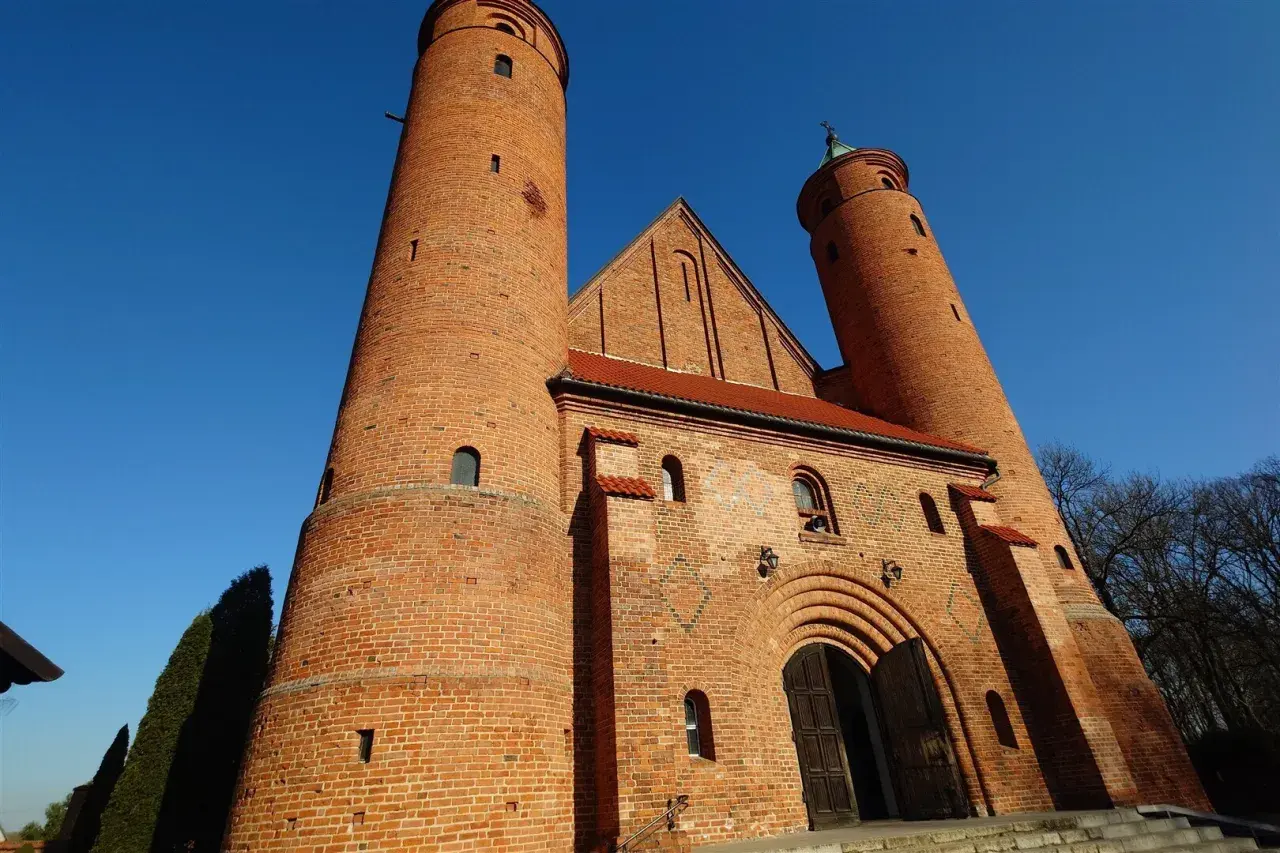 Imponująca ceglana świątynia w Brochowie z dwiema wieżami i łukowym portalem, pod błękitnym niebem.