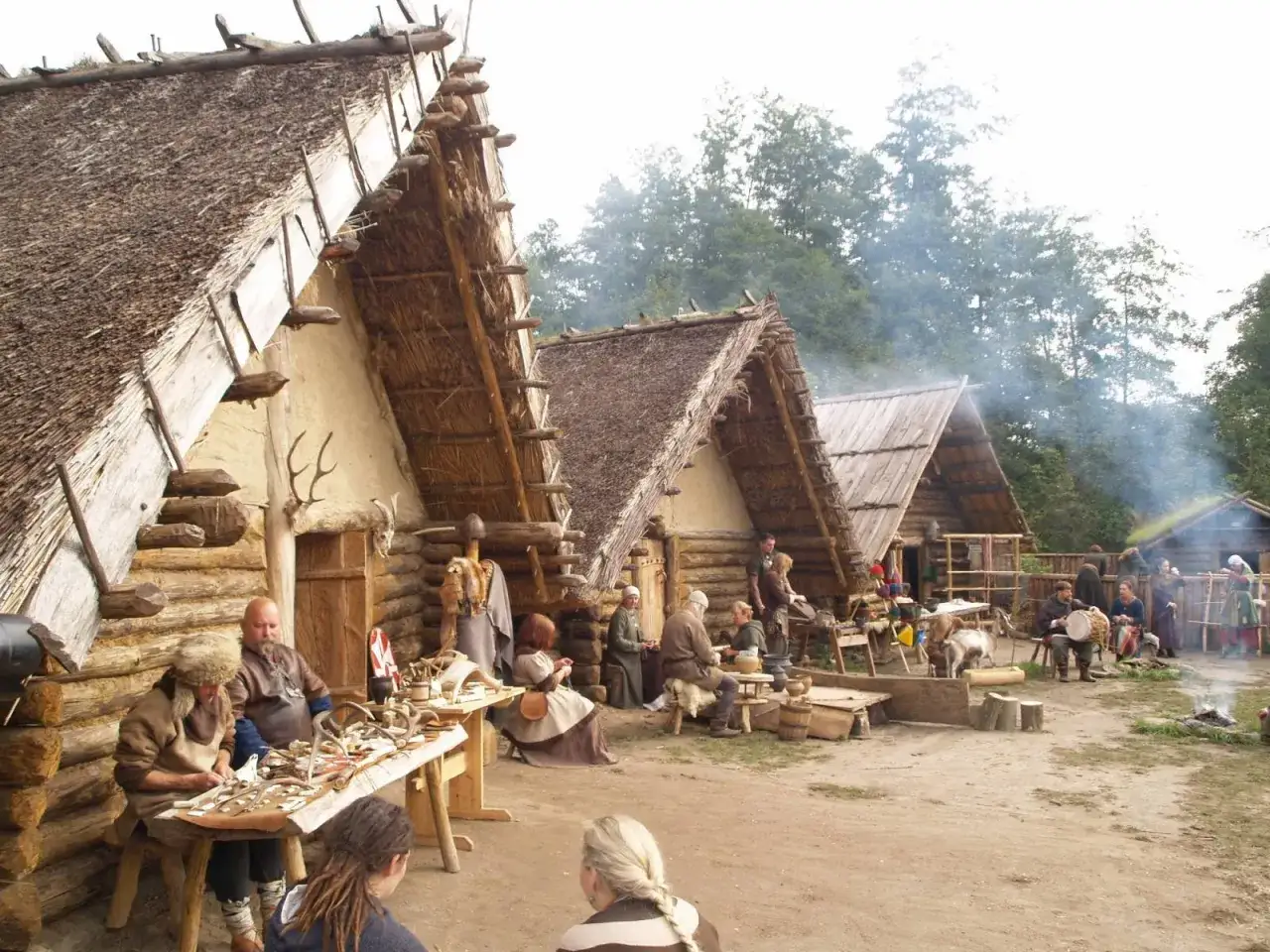 Odwzorowana osada Biskupin z chatami krytymi strzechą i ludźmi w strojach z epoki.