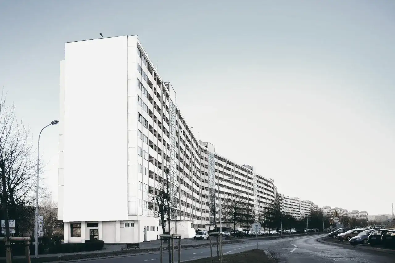 Długi, biały blok mieszkalny, prawdopodobnie najdłuższy blok w Polsce, ciągnie się wzdłuż ulicy. Widać wiele okien i balkonów.