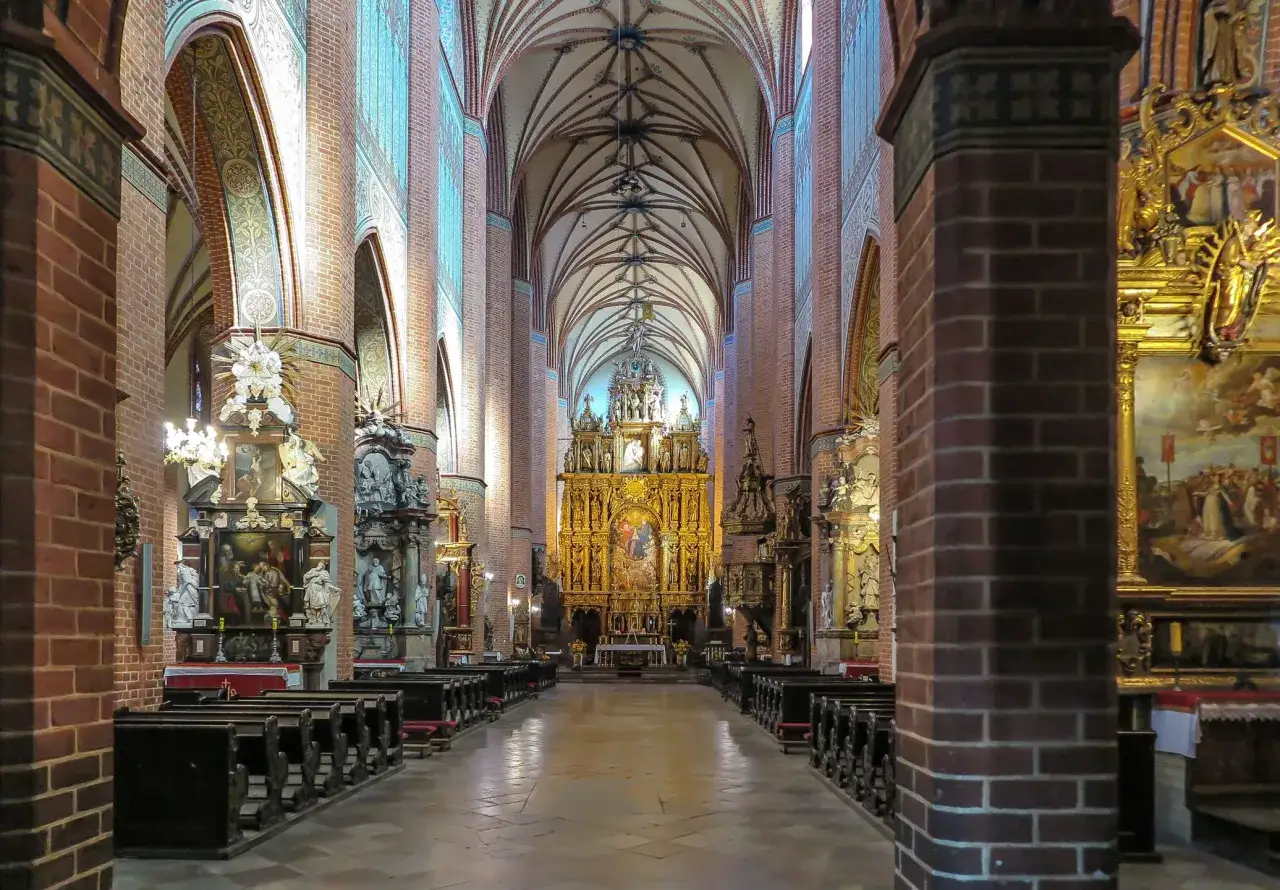 Wnętrze katedry w Pelplinie z ołtarzem głównym i rzędami ławek.