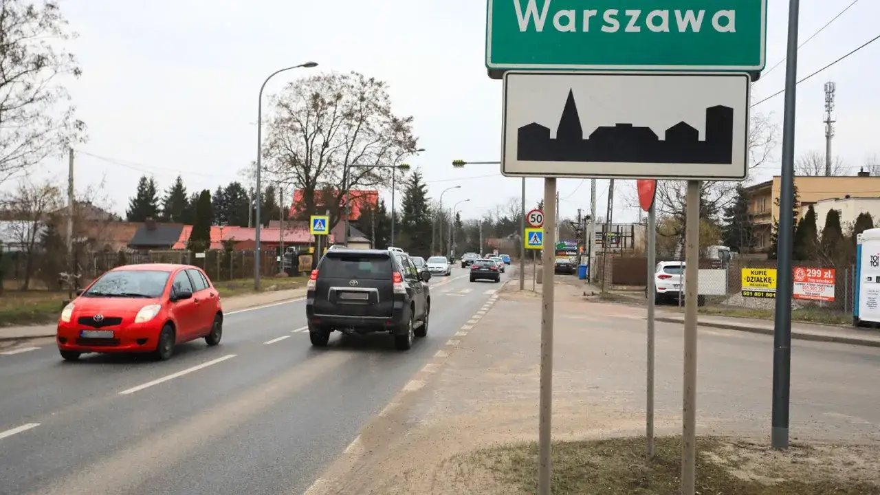 Wjazd do Warszawy, miasta z najdłuższą ulicą w Polsce. Samochody jadą drogą, mijając znak z panoramą stolicy.