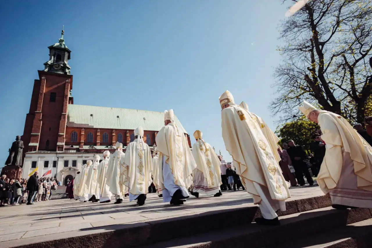 Uroczysty pochód duchownych w bogato zdobionych szatach przed katedrą, przypominający scenę z koronacji Bolesława Chrobrego.