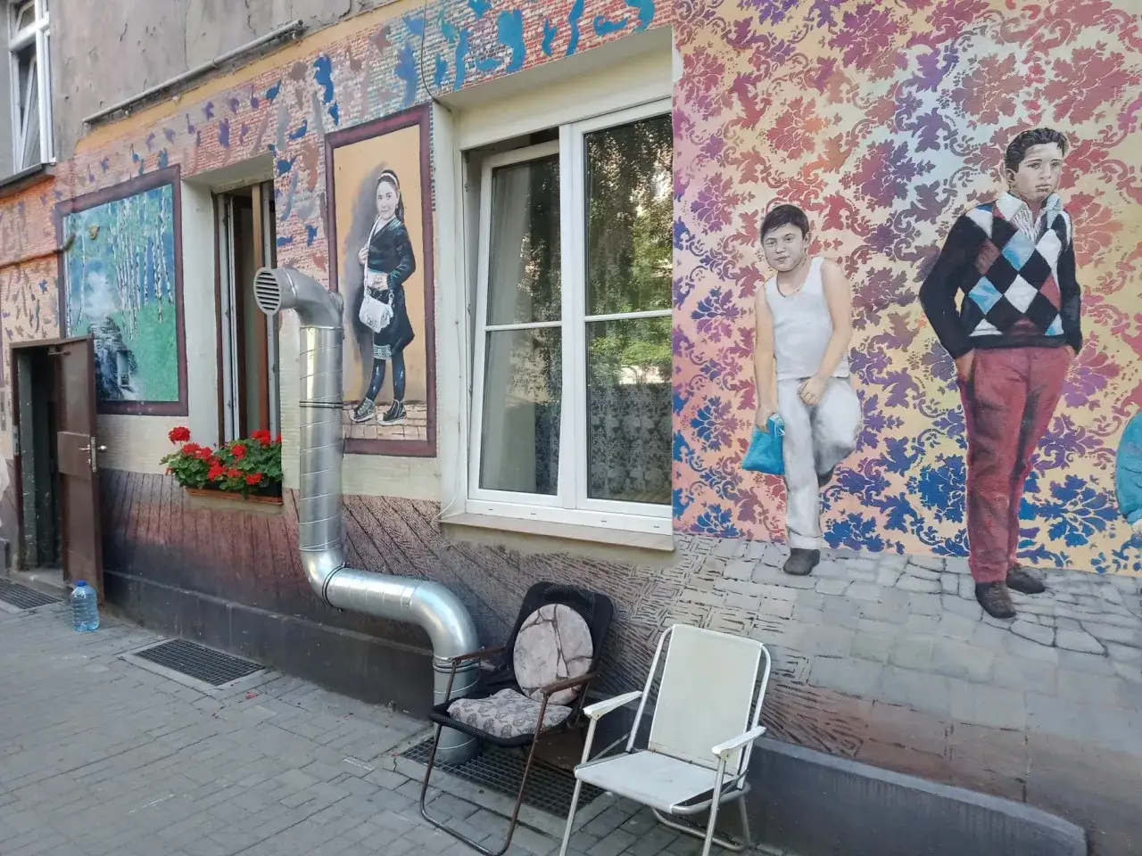 Kolorowe murale na Nadodrzu zdobią ścianę kamienicy. Dzieci na obrazach wyglądają jakby czekały na kogoś.