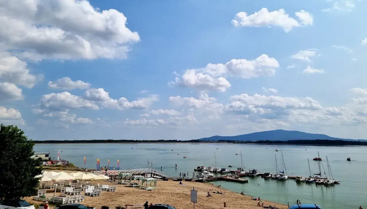 Słoneczny dzień nad zalewem Mietkowskim. Łodzie kołyszą się przy pomoście, a na plaży odpoczywają ludzie.