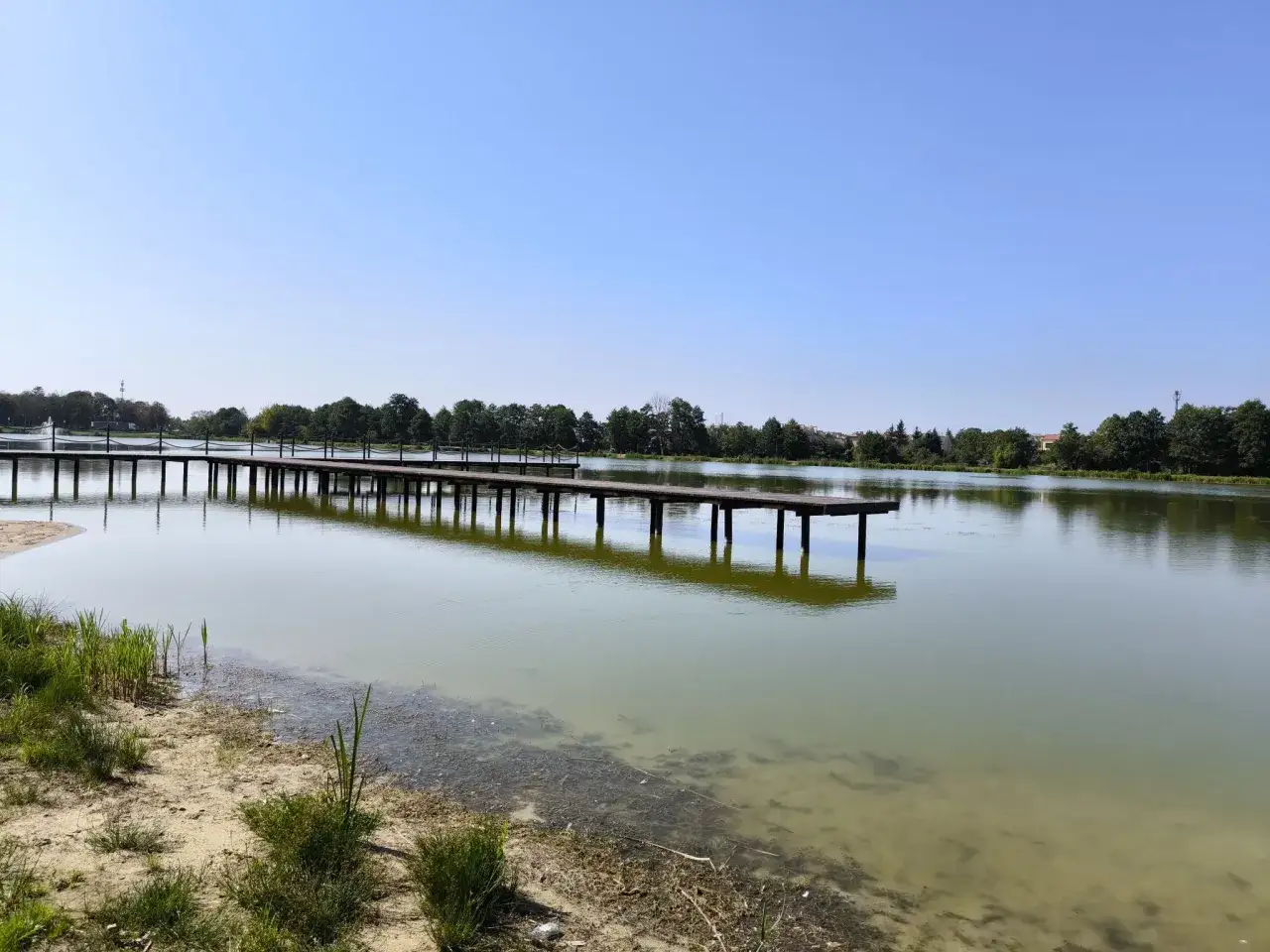 Długie molo nad jeziorem w Krasnosielcu, otoczone zielenią i błękitnym niebem.