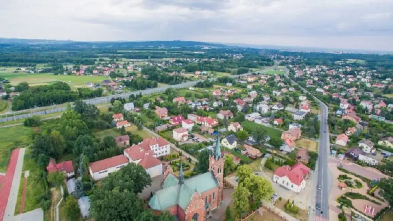 Widok z lotu ptaka na Wola Rzędzińska: kościół, domy z czerwonymi dachami, droga i tereny zielone.