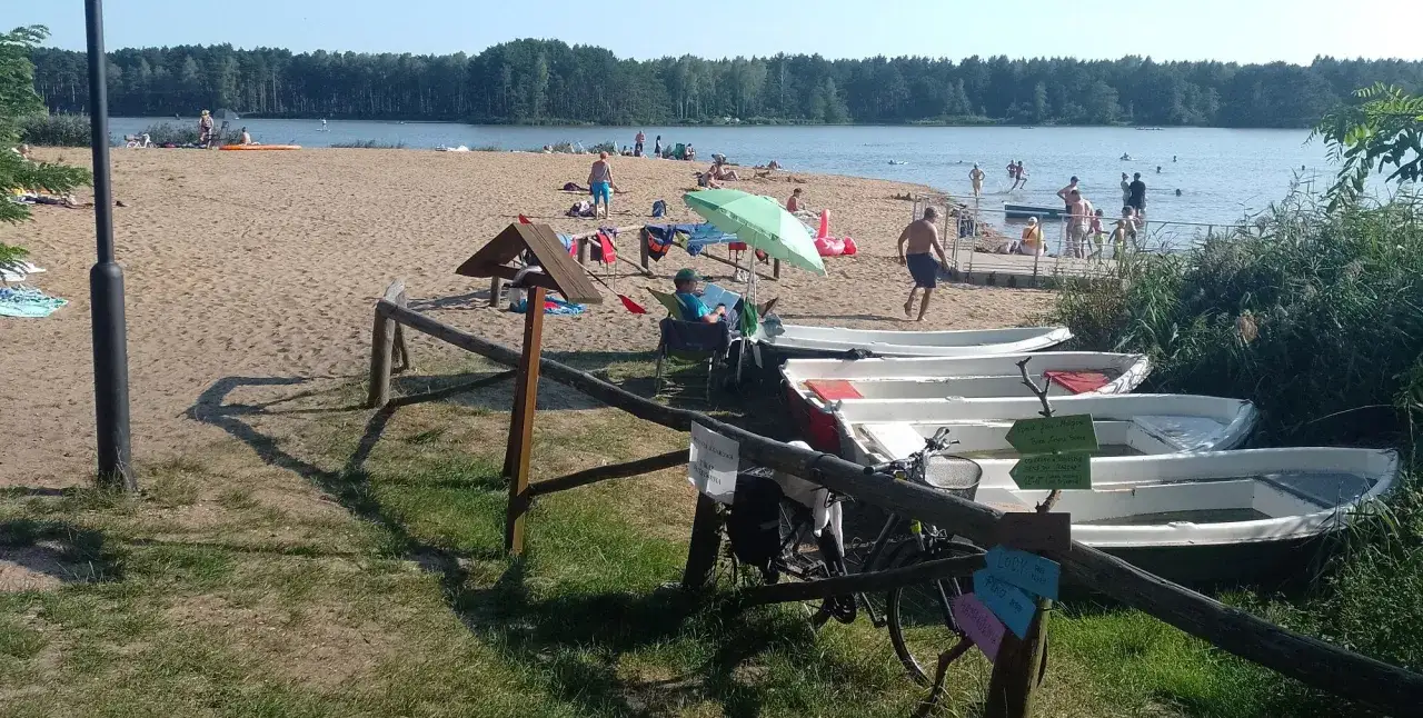 Słoneczny dzień nad zalewem zielona. Ludzie odpoczywają na plaży, kąpią się, a obok cumują łódki.