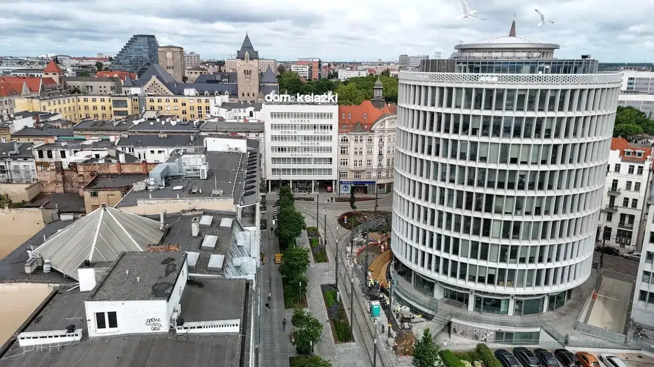Okrągły budynek w Poznaniu, obok Domu Książki, z widokiem na miasto i dwa mewy w locie.