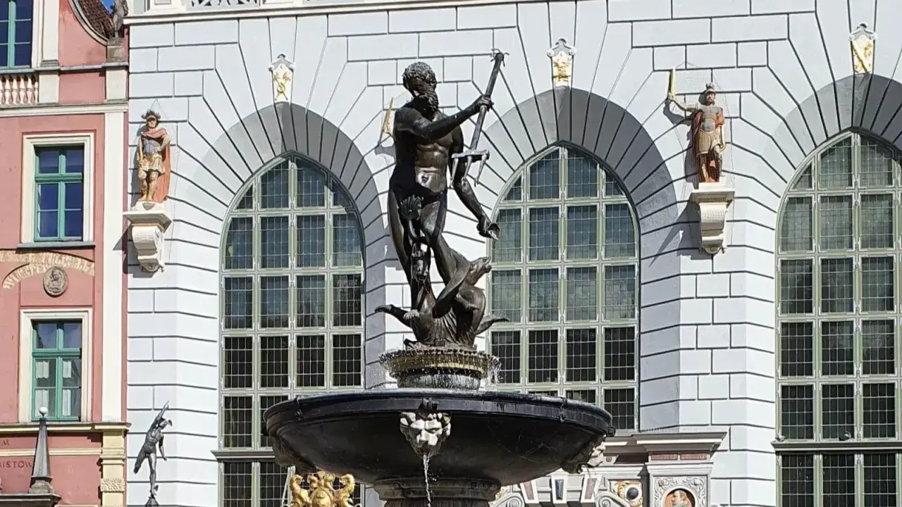 Fontanna Neptuna znajduje się w Gdańsku, przed fasadą budynku z arkadowymi oknami. Rzeźba przedstawia boga mórz na tle kamiennej budowli.