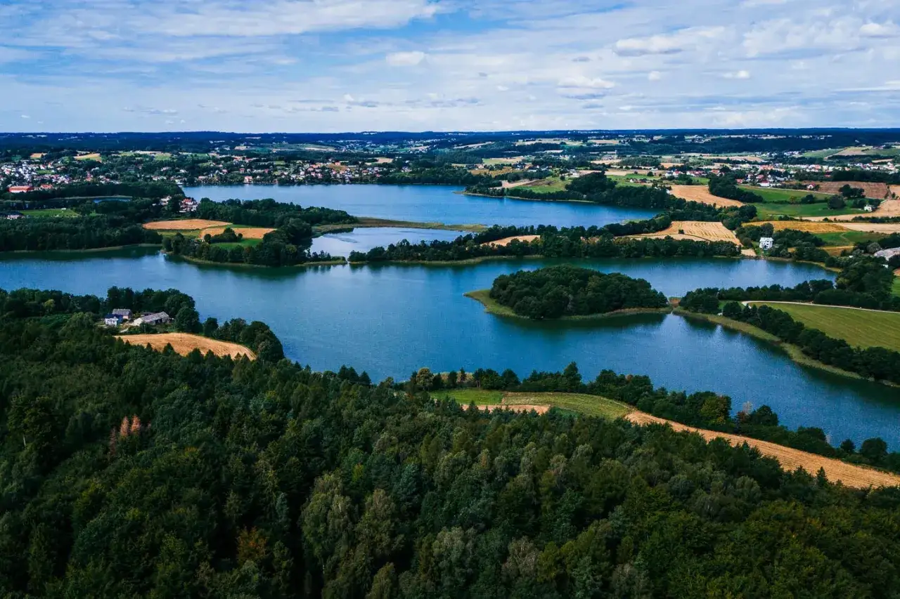 Malownicze jeziora i lasy, gdzie są Kaszuby. Widok z lotu ptaka na zielone wzgórza, pola i zabudowania.
