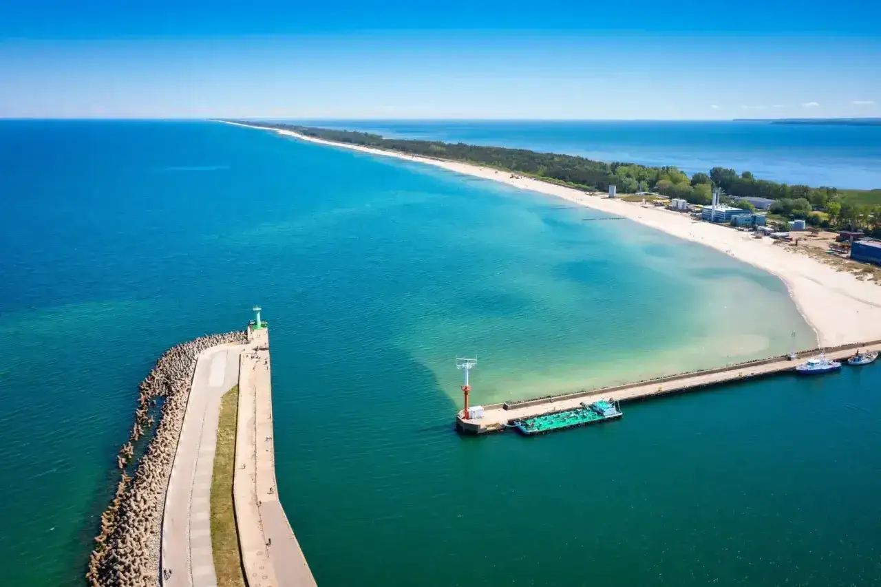 Dwa falochrony chroniące wejście do portu, z latarniami morskimi i statkami. Piękna plaża i turkusowa woda.