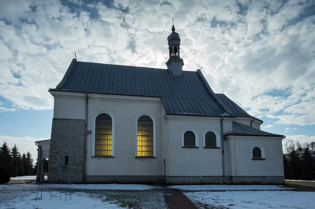 Kościół w Dulczy Wielkiej z żółtym światłem w oknach, na tle pochmurnego nieba.