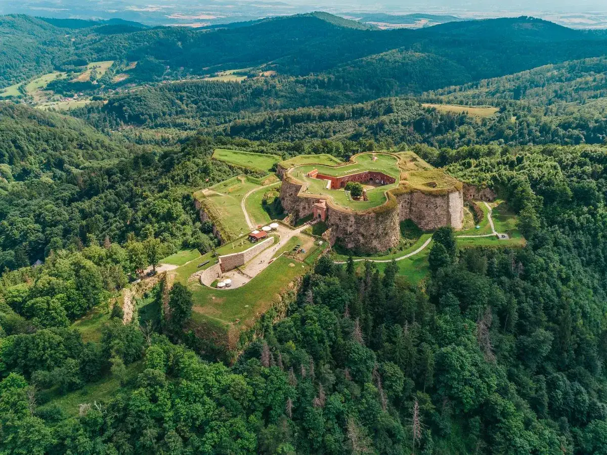 Forteca na wzgórzu, otoczona lasem. Srebrna Góra oferuje wspaniałe atrakcje historyczne i widokowe.