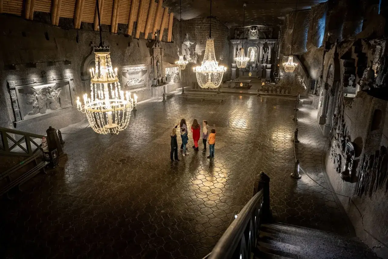 Wielka komnata w kopalni soli w Wieliczce z kryształowymi żyrandolami. Grupa turystów podziwia rzeźby. Sprawdź kopalnia soli wieliczka cennik.