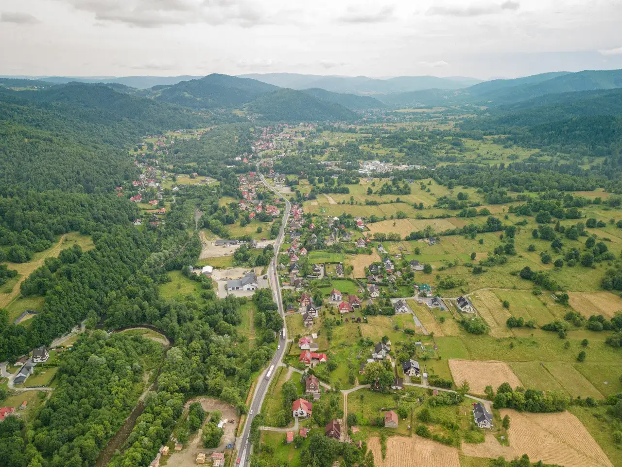 Widok z lotu ptaka na malowniczą dolinę z krętą rzeką i zabudowaniami rozciągającymi się wzdłuż drogi. To krajobraz, który może przypominać najdłuższą wieś w Polsce.