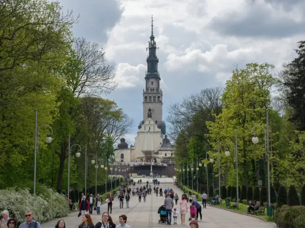 Aleja prowadząca do Jasnej Góry, jednego z najważniejszych sanktuariów maryjnych w Polsce. Ludzie spacerują w kierunku imponującej wieży klasztornej.